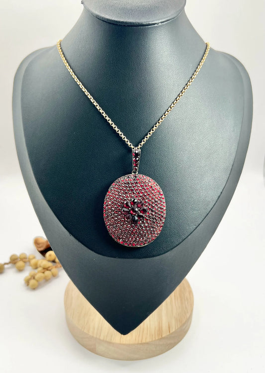 An antique oval locket encrusted with garnets, with a chain, on a black bust