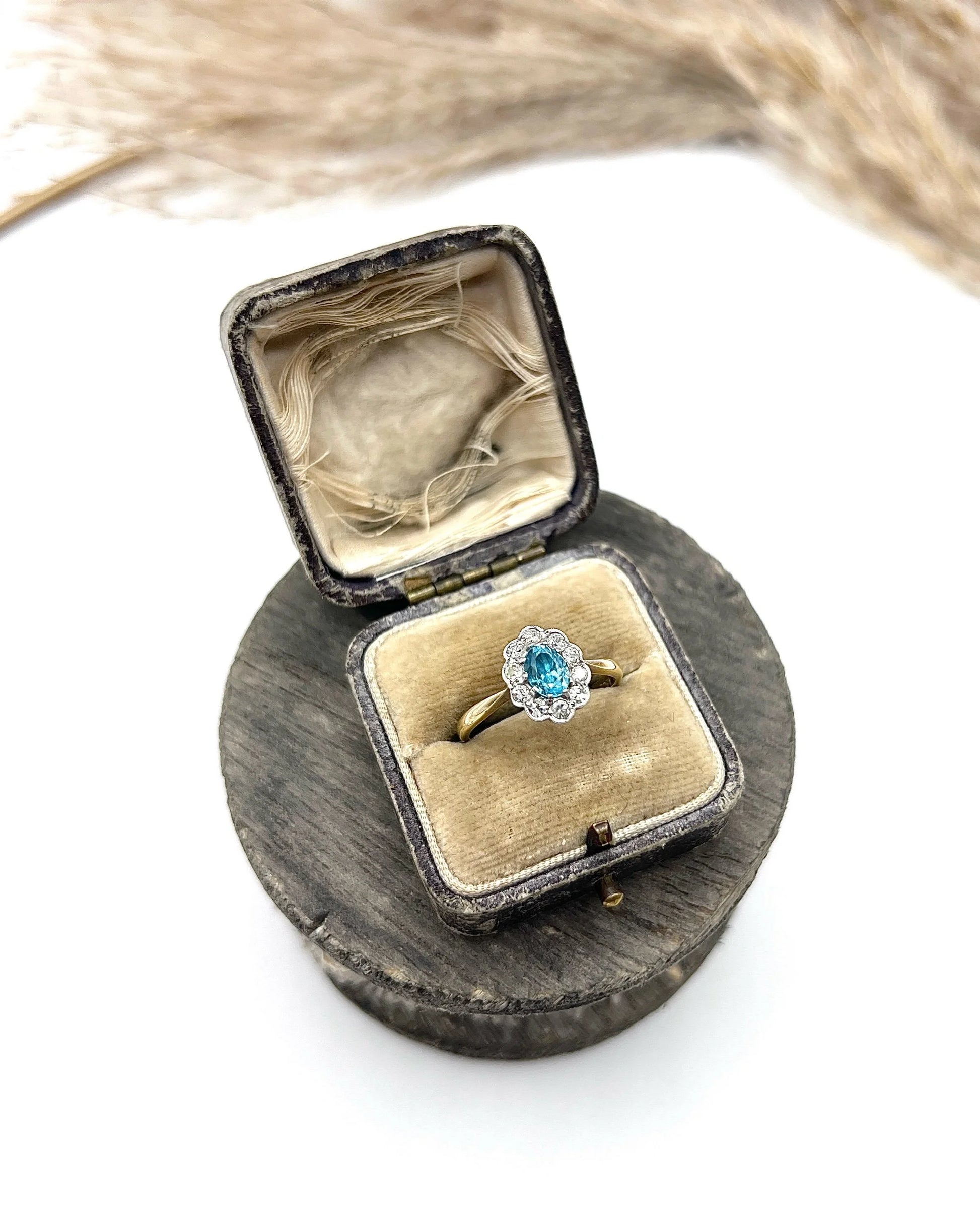 An oval cluster ring with a blue zircon centre surrounded by round diamonds, in yellow gold and platinum, in an antique ring box