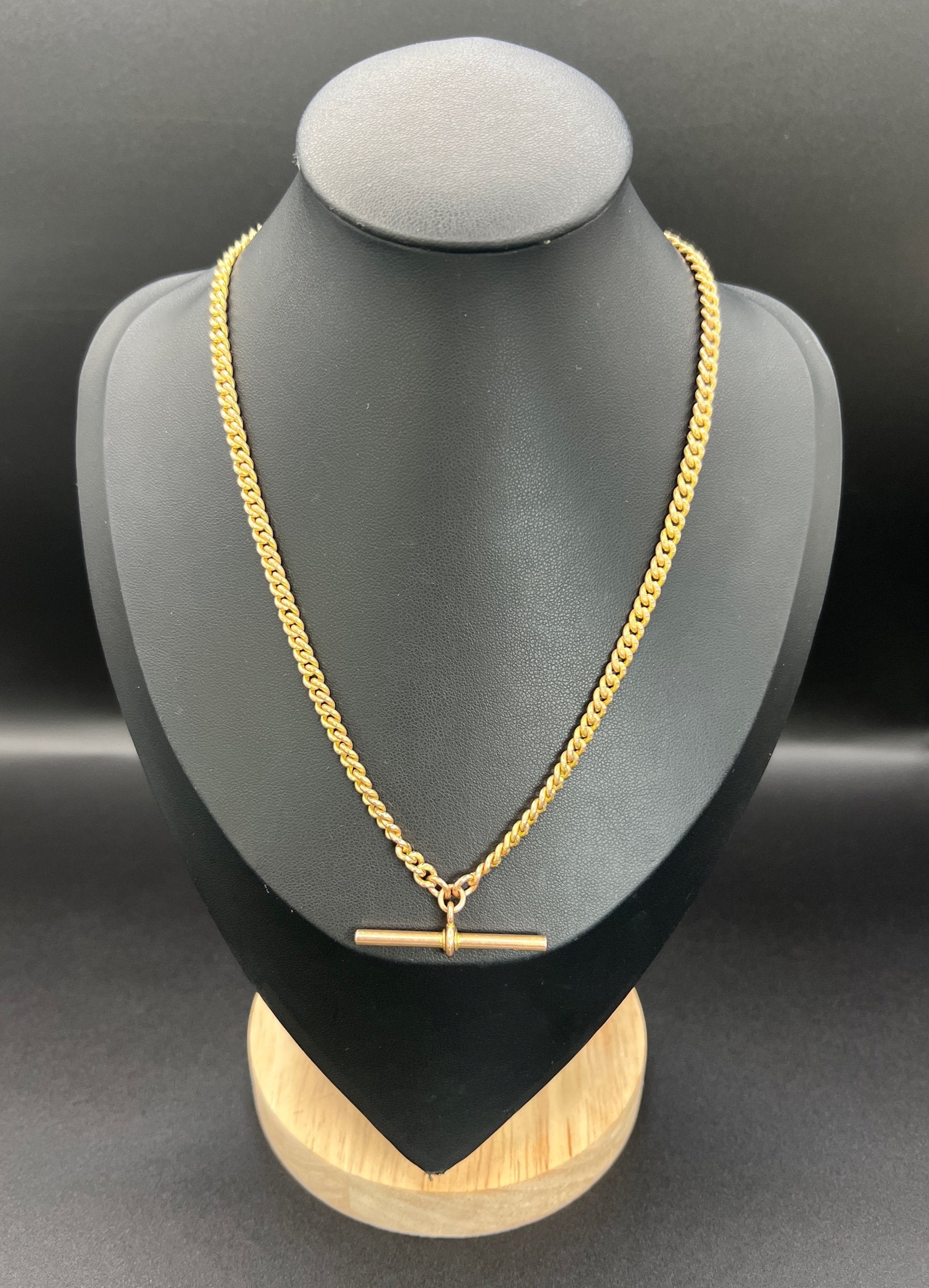 A yellow gold curb link Albert watch chain, on a black jewellery bust