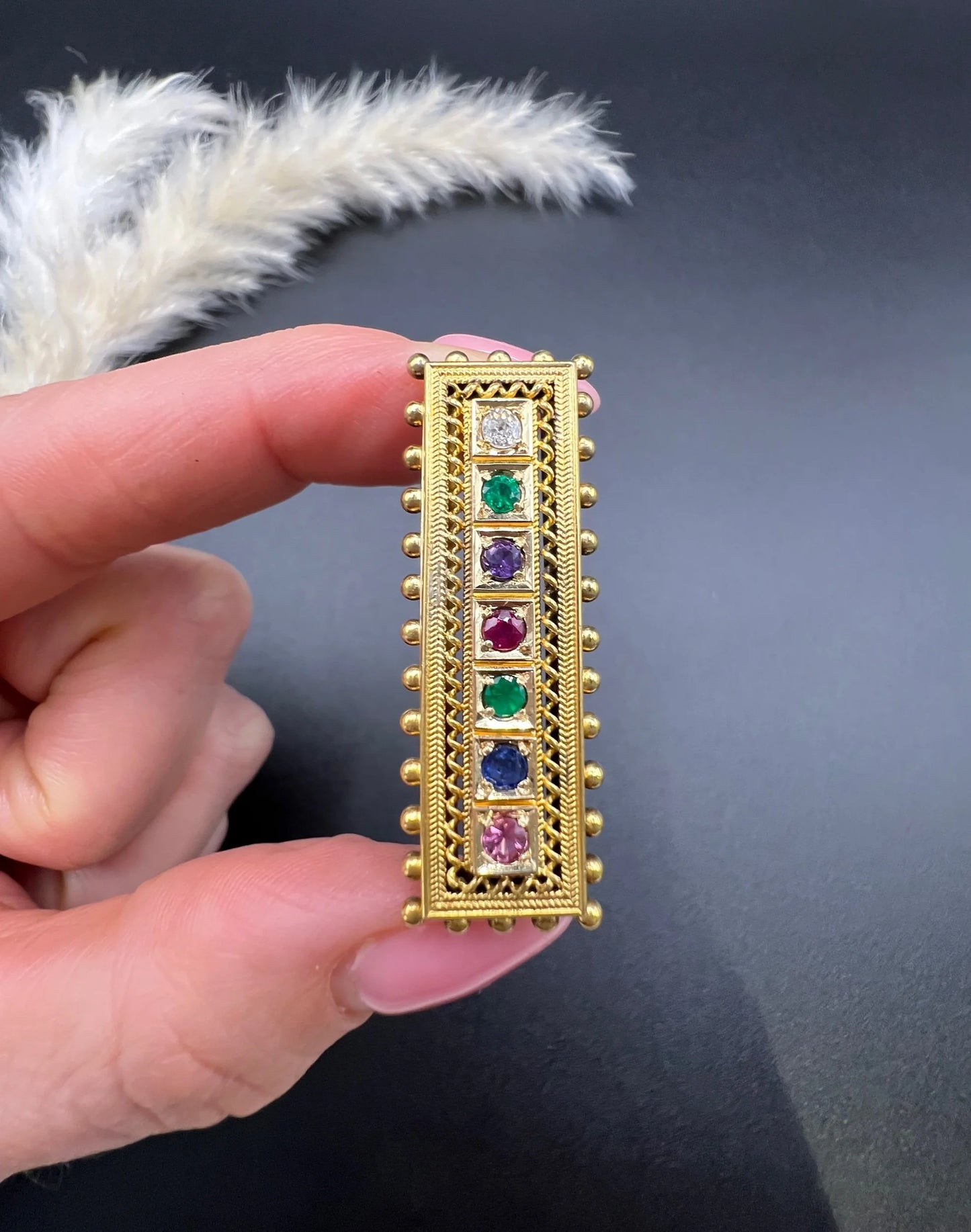 A yellow gold multi-gemstone and diamond acrostic brooch, held in a hand