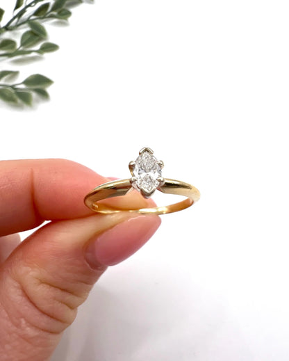 A marquise diamond solitaire ring in yellow and white gold, held in a hand