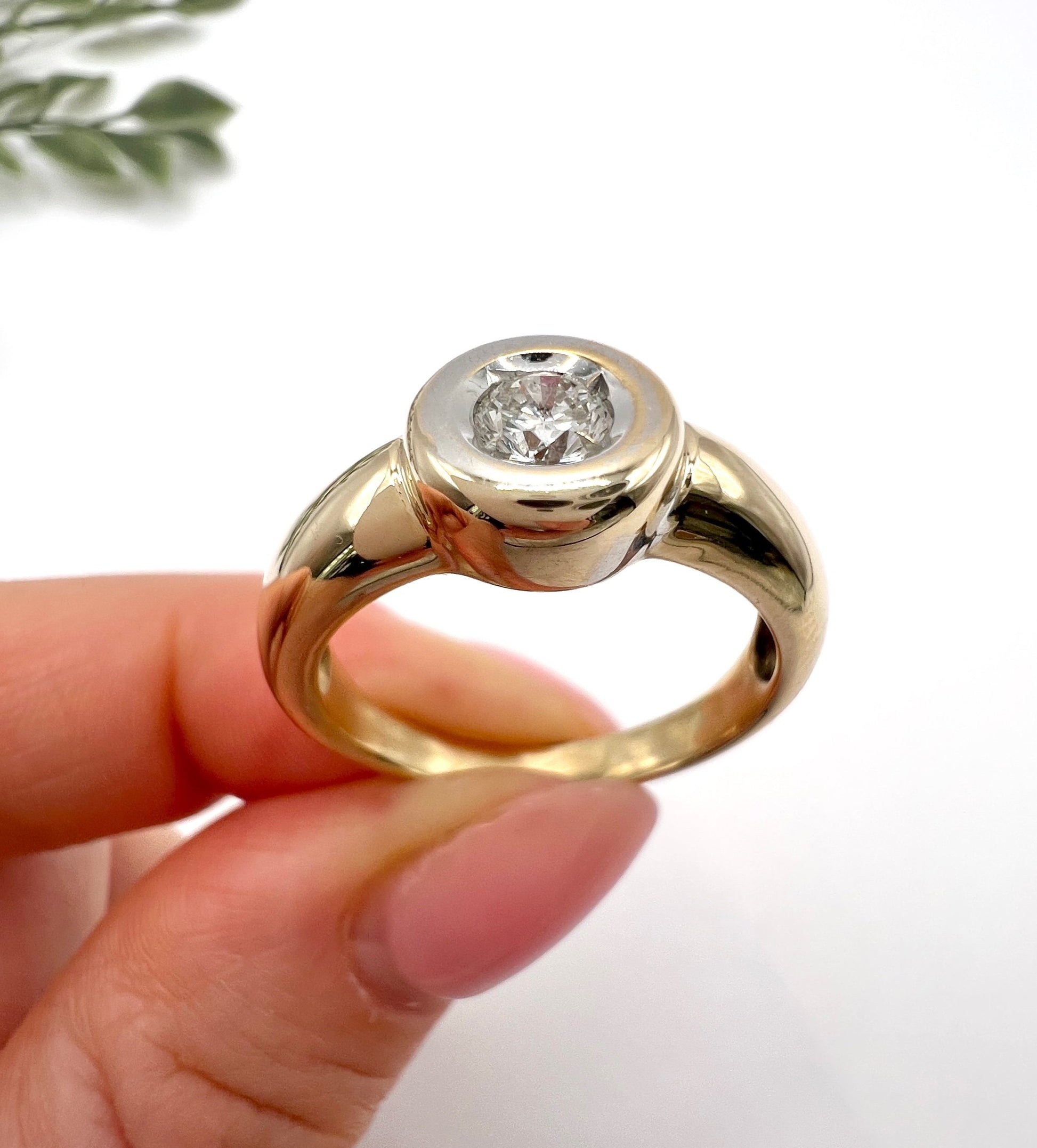 A single stone brilliant cut diamond ring bezel set in yellow gold, held in a hand