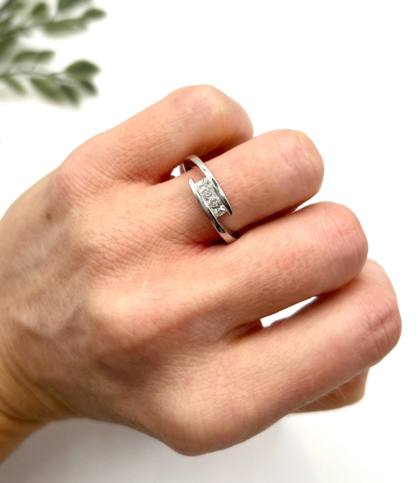 A three stone princess cut diamond crossover ring in white gold, modelled on a hand
