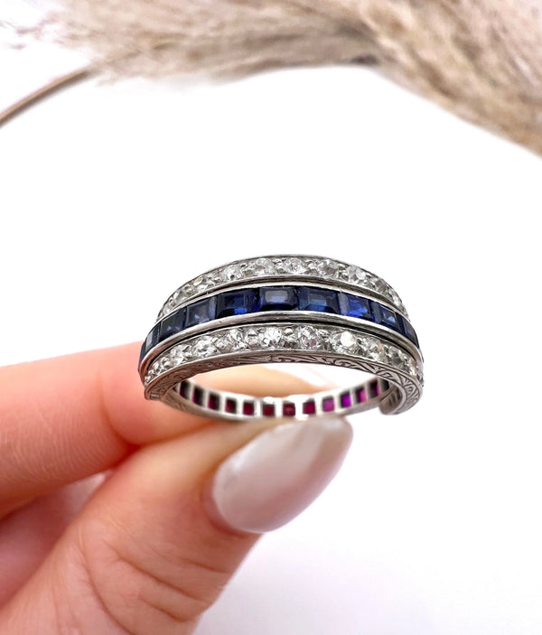 A platinum night and day flip band ring set with diamonds, sapphires and rubies, held in a hand