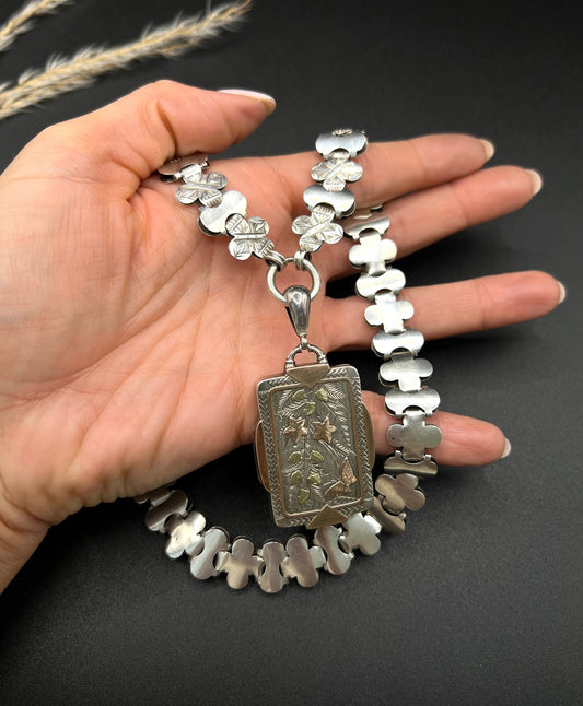 An antique rectangular locket with gold inlay, on a book collar necklace, held in a hand