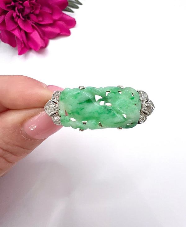 A carved green jade and diamond brooch in white gold, held in a hand