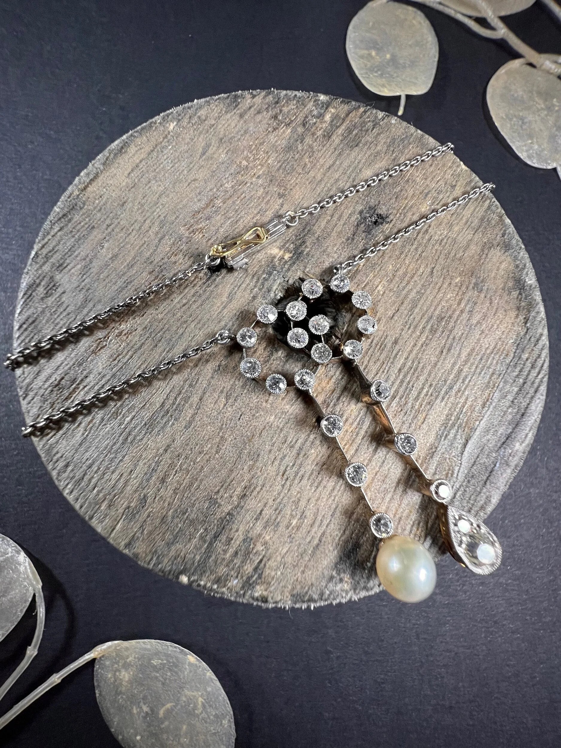 An antique diamond and pearl double drop pendant necklace, on a wooden spool