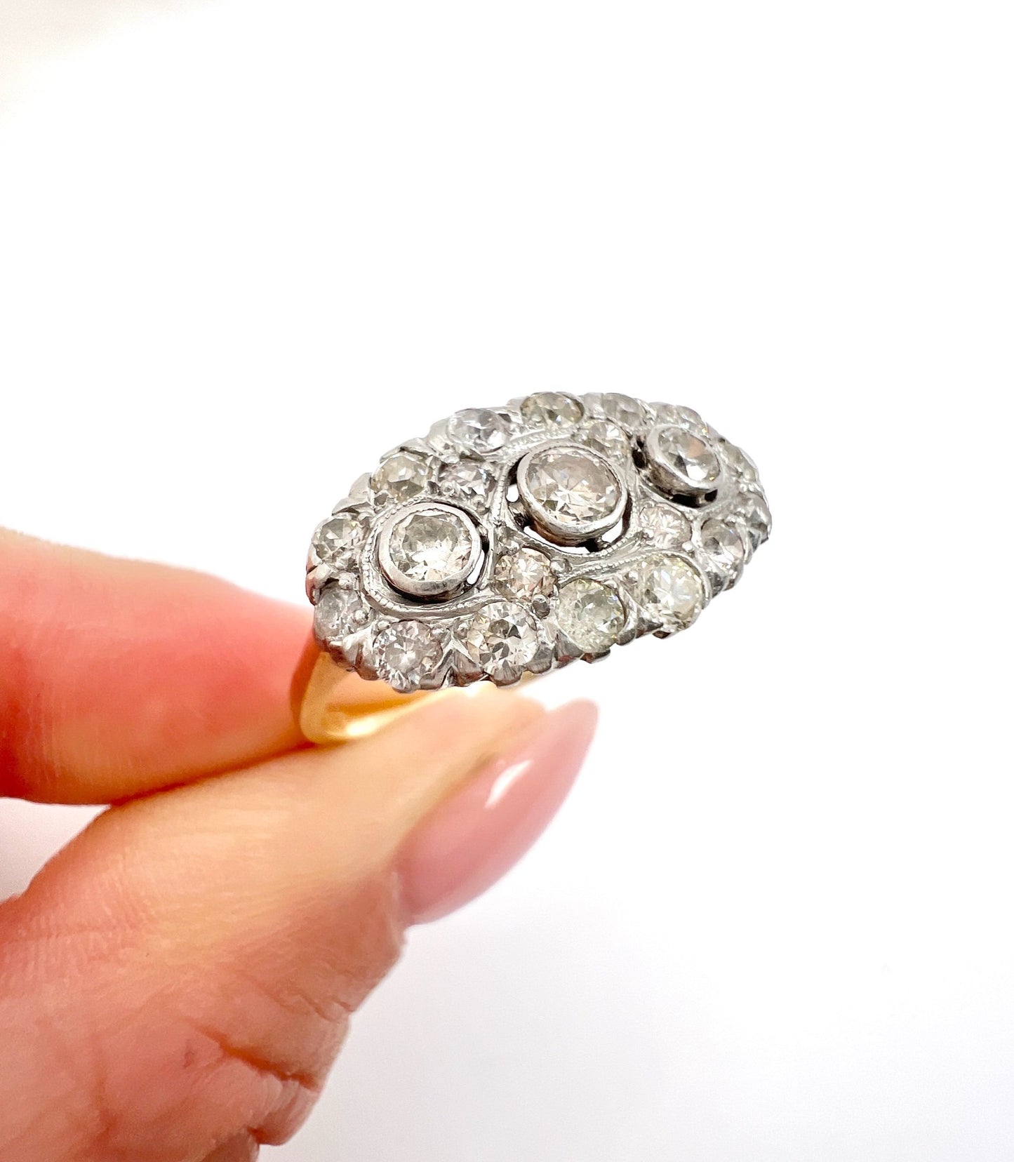 A diamond triple cluster ring in yellow and white gold, held in a hand