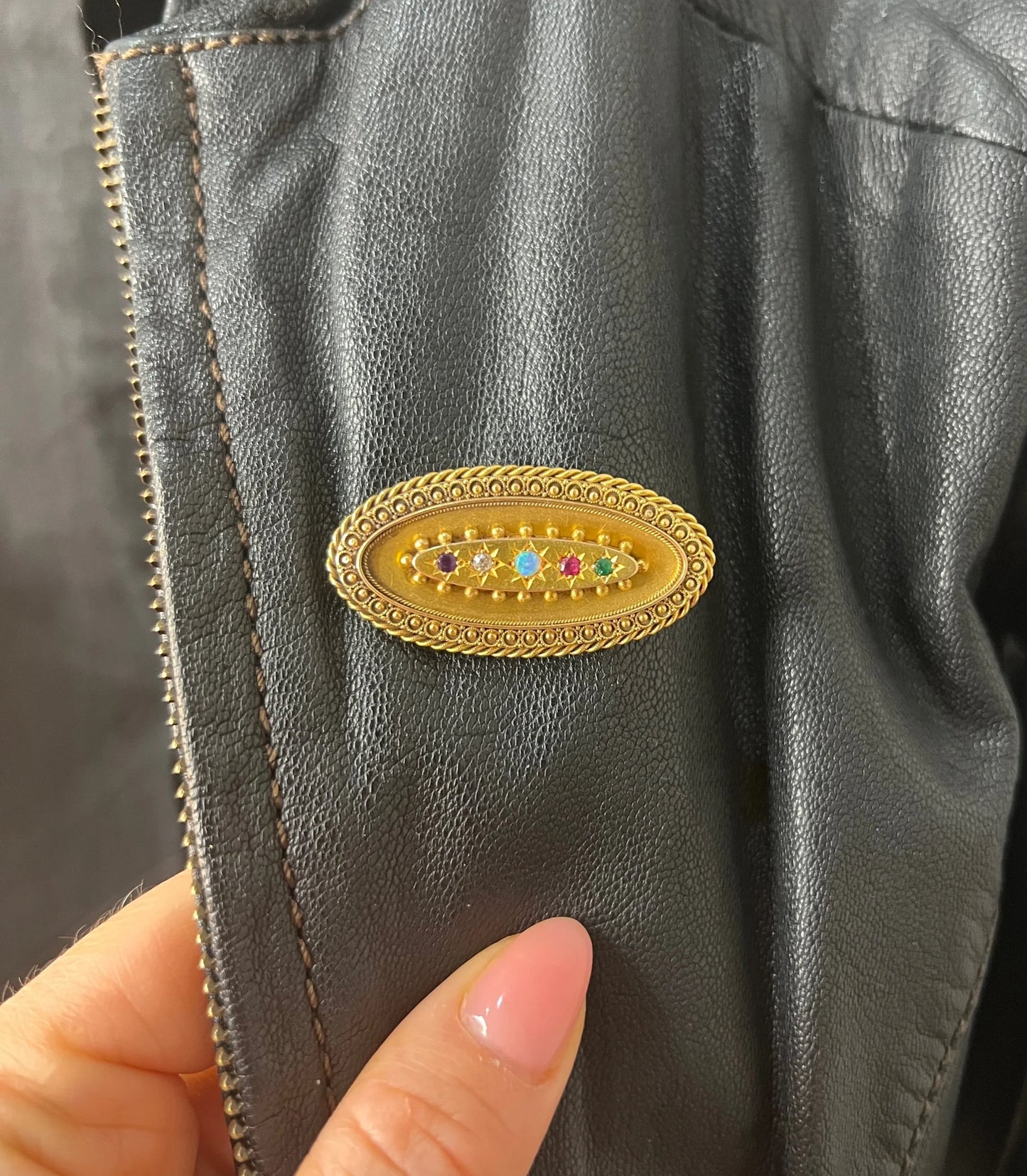 An oval yellow gold multi-gemstone acrostic brooch, modelled on a black leather jacket