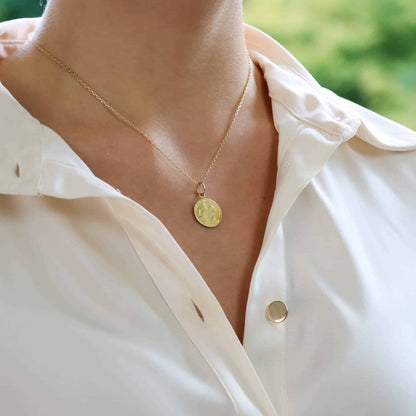 A yellow gold saint christopher pendant modelled on a gold chain by a woman wearing a white shirt