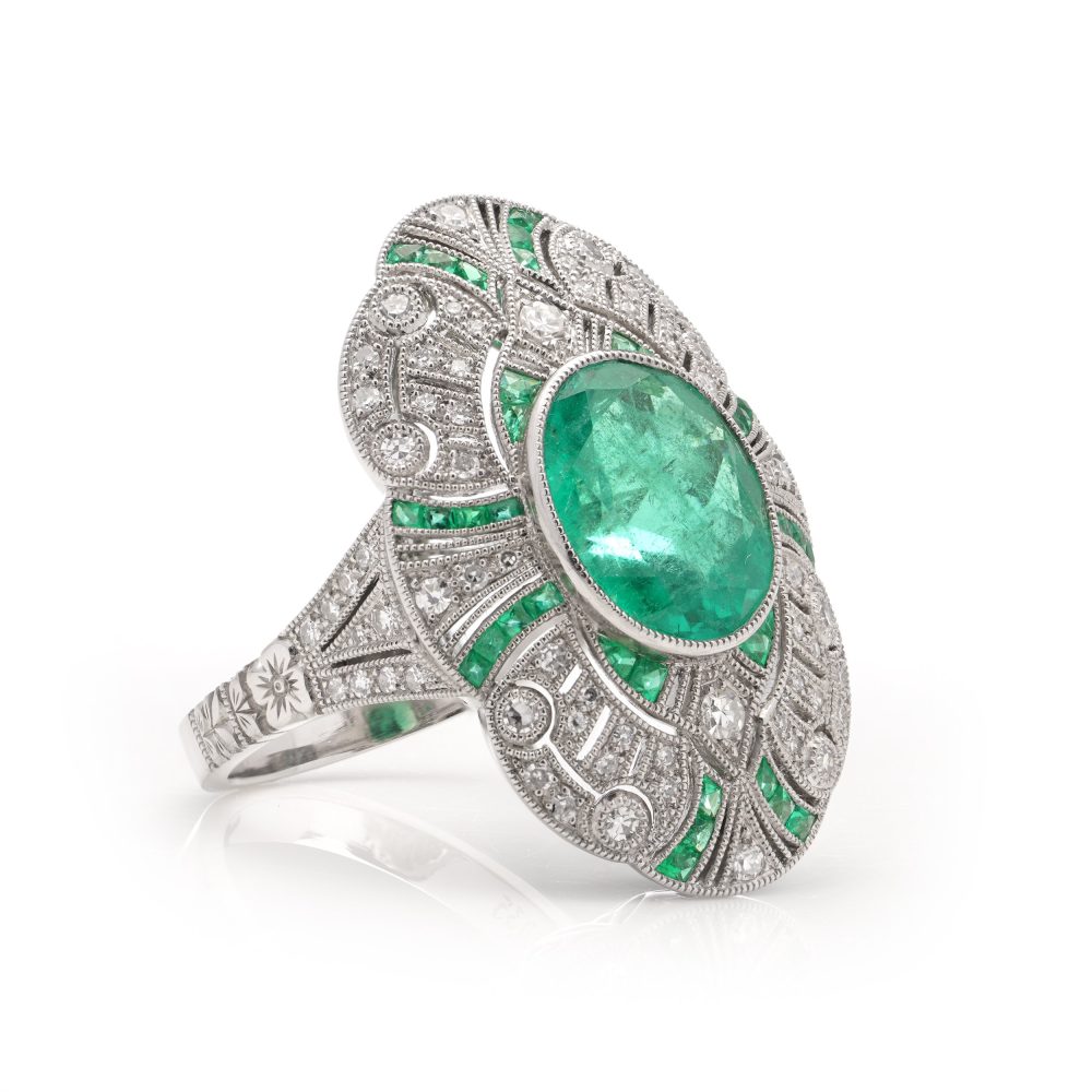 Oval cut emerald ring surround by emeralds and diamonds set in platinum.