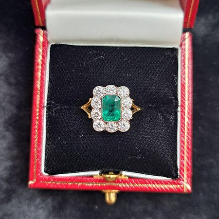 An emerald and diamond rubover set cluster ring in yellow and white gold, in a red ring box