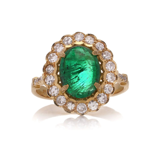 A yellow gold ring with an oval emerald surrounded by round diamonds, on a white background