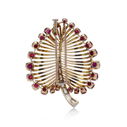 A gold and platinum leaf shaped brooch with baguette cut diamonds and cabochon cut rubies, on a white background