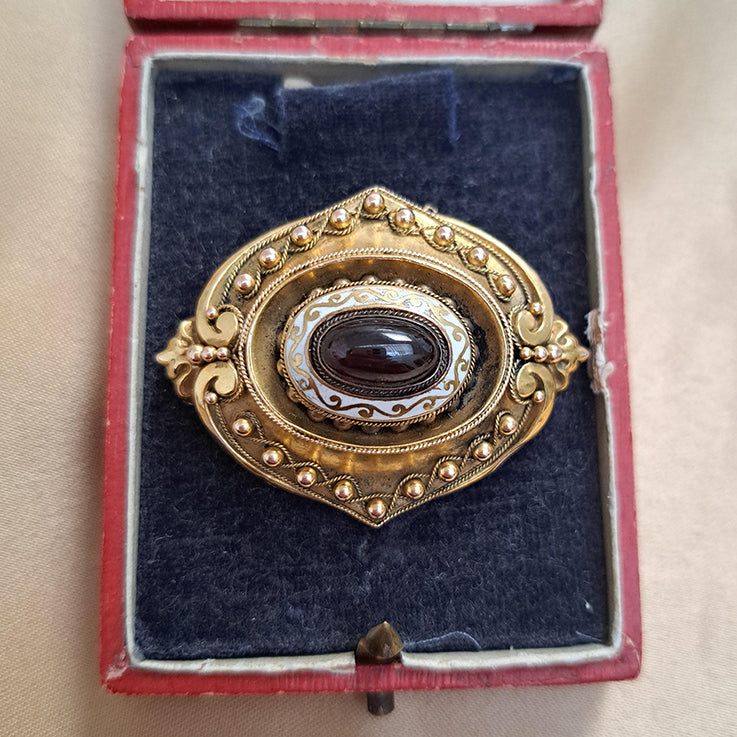 Antique Cabochon Garnet and Gold Locket Brooch, decorative 18ct yellow gold brooch with ball and ropework detailing with central oval cabochon garnet surrounded by white enamel. With locket compartment to reverse