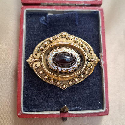 Antique Cabochon Garnet and Gold Locket Brooch, decorative 18ct yellow gold brooch with ball and ropework detailing with central oval cabochon garnet surrounded by white enamel. With locket compartment to reverse