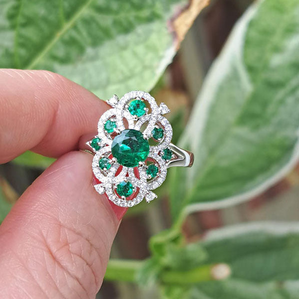 Decorative 1.13ct Emerald and Diamond Cluster Dress Ring, 1.13 carat emerald nestled within entwinned loop diamond surround with emerald accents in 18ct white gold