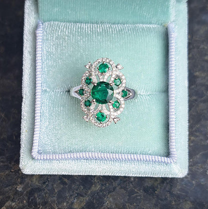 Decorative 1.13ct Emerald and Diamond Cluster Dress Ring, 1.13 carat emerald nestled within entwinned loop diamond surround with emerald accents in 18ct white gold