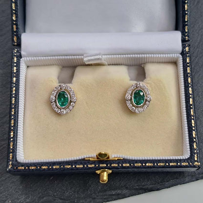 A pair of oval emerald and brilliant cut diamond oval cluster stud earrings in yellow and white gold, in an earring box
