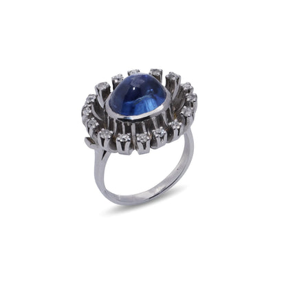 A cabochon blue sapphire and diamond ring in platinum, on a white background