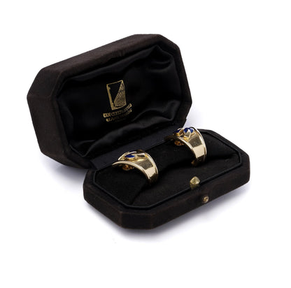 A pair of yellow gold earrings with blue enamel leaves and round diamonds, in a black box, on a white background