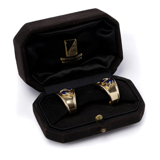 A pair of yellow gold earrings with blue enamel leaves and round diamonds, in a black box, on a white background