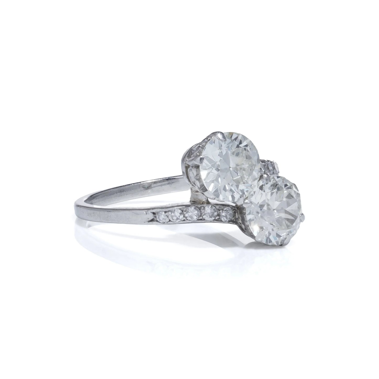 A two stone diamond crossover ring in white gold with diamond shoulders, on a white background
