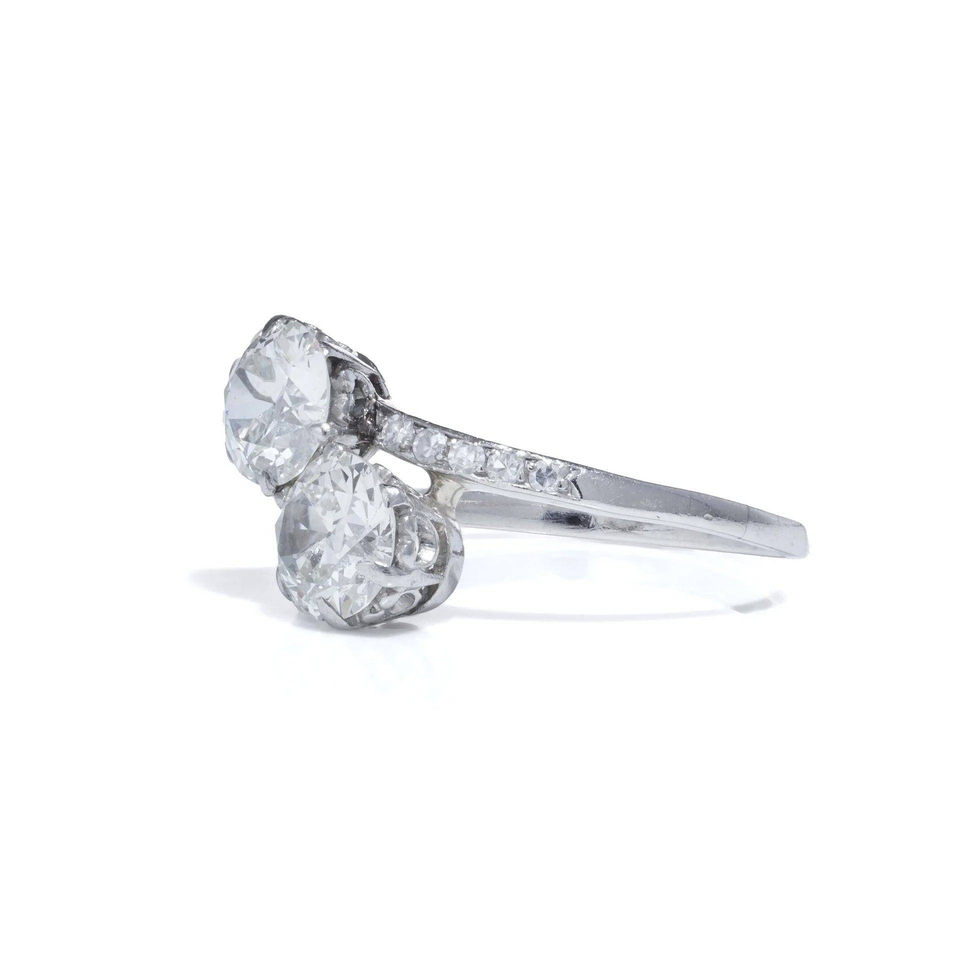 A two stone diamond crossover ring in white gold with diamond shoulders, on a white background