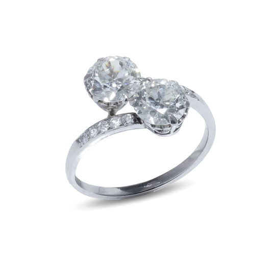 A two stone diamond crossover ring in white gold with diamond shoulders, on a white background