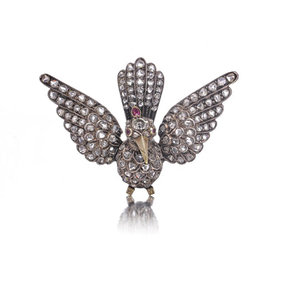 An antique bird in flight brooch set with diamonds and rubies, in silver and gold, on a white background
