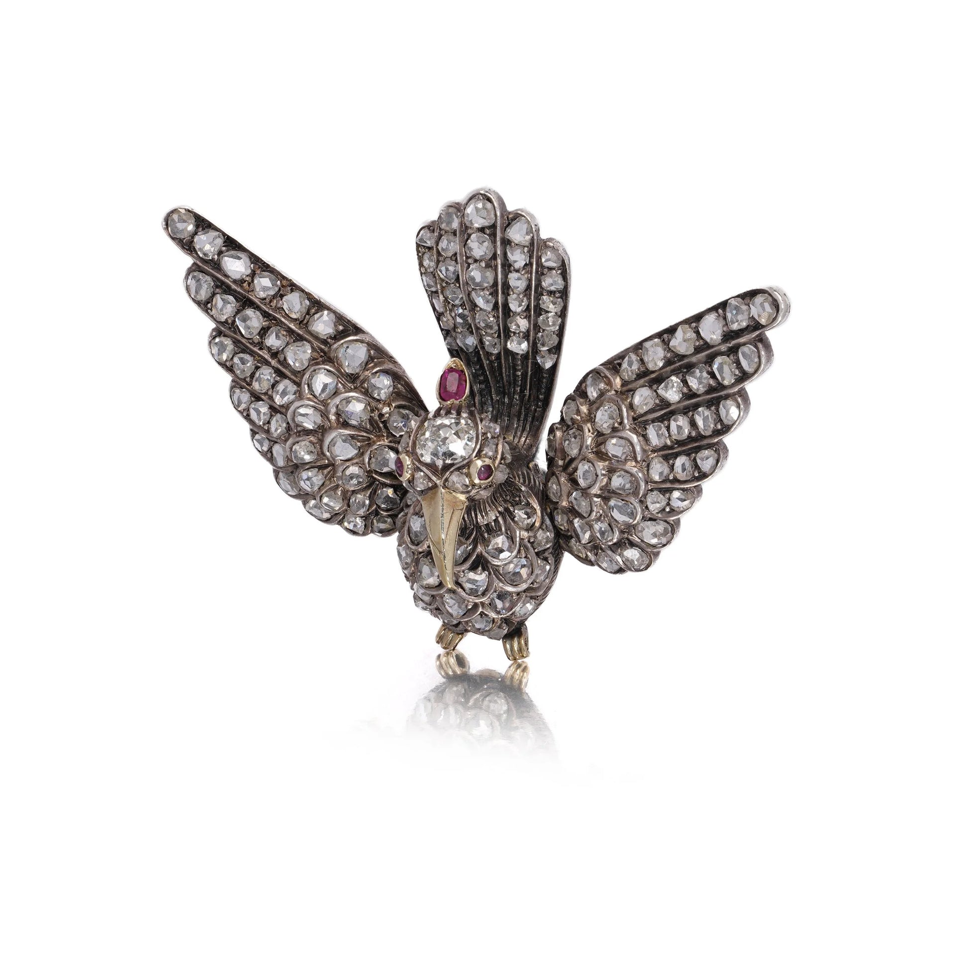 An antique bird in flight brooch set with diamonds and rubies, in silver and gold, on a white background