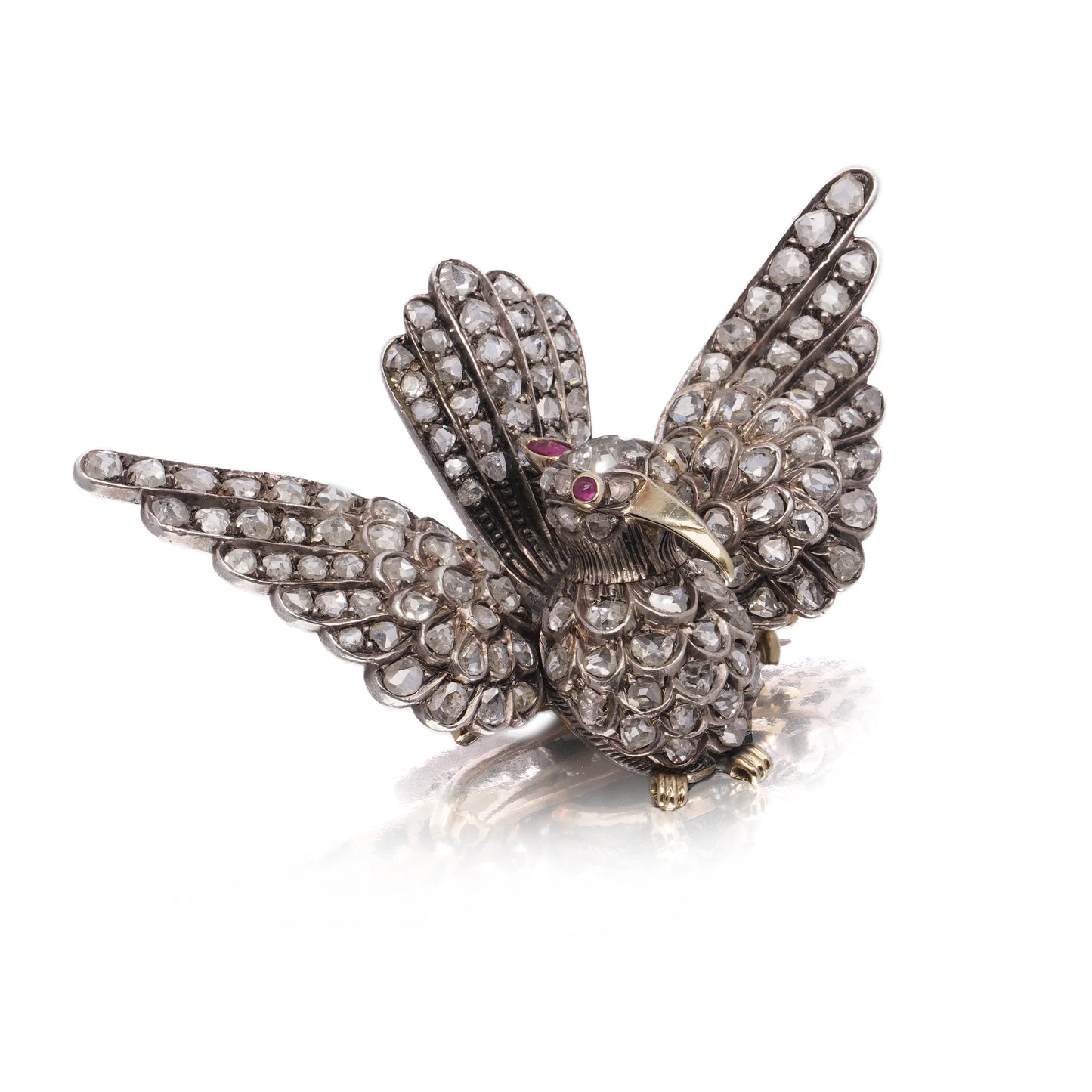 An antique bird in flight brooch set with diamonds and rubies, in silver and gold, on a white background