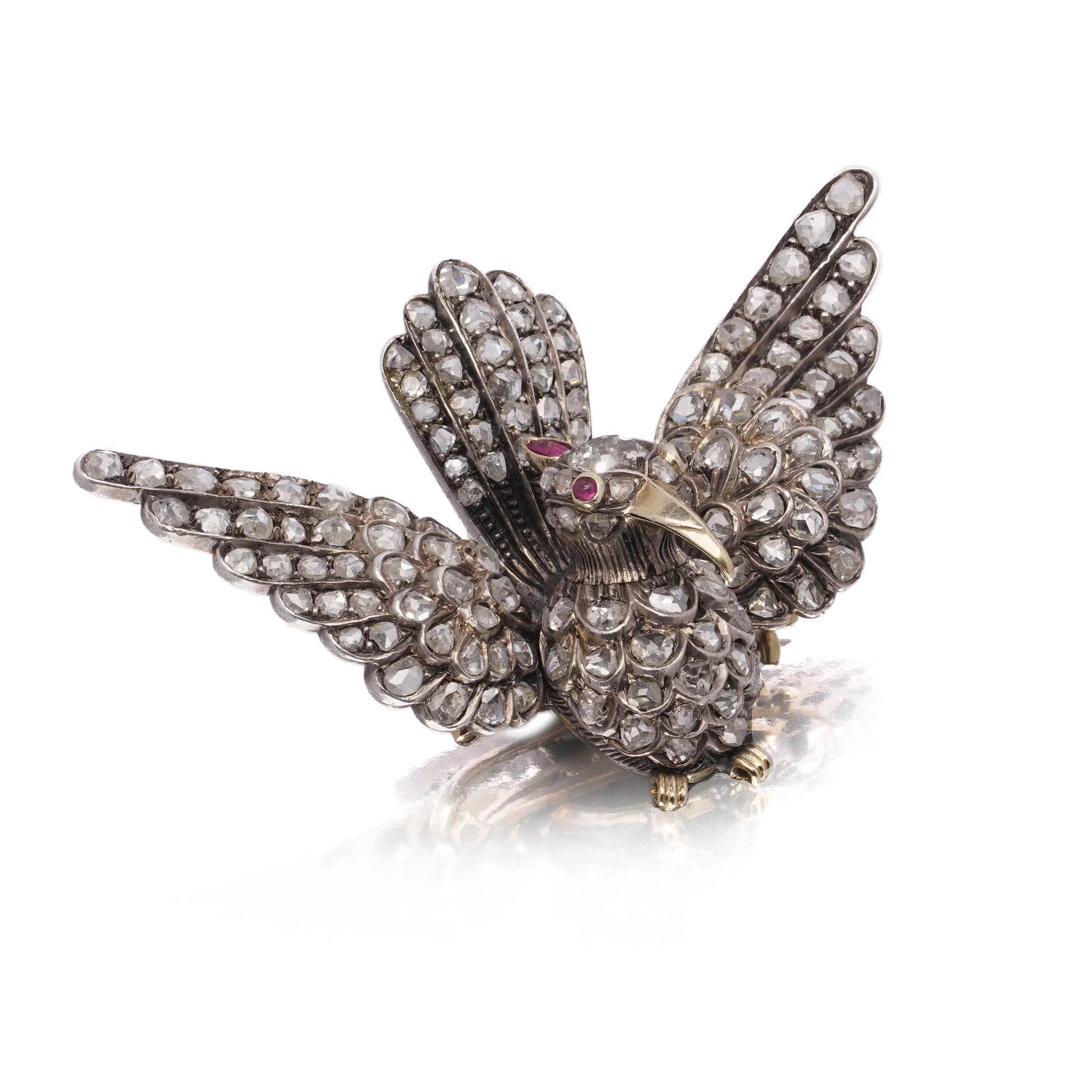 An antique bird in flight brooch set with diamonds and rubies, in silver and gold, on a white background