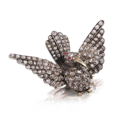 An antique bird in flight brooch set with diamonds and rubies, in silver and gold, on a white background