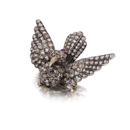 An antique bird in flight brooch set with diamonds and rubies, in silver and gold, on a white background