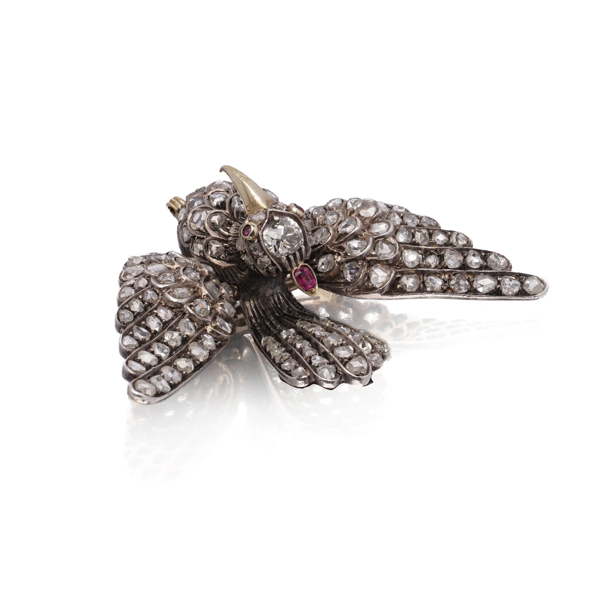 An antique bird in flight brooch set with diamonds and rubies, in silver and gold, on a white background