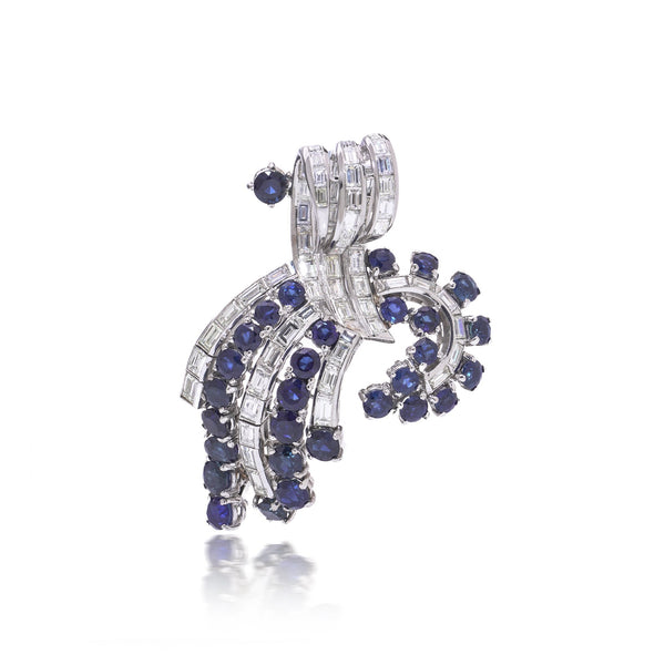 A decorative baguette cut diamond and round sapphire brooch in white metal, on a white background