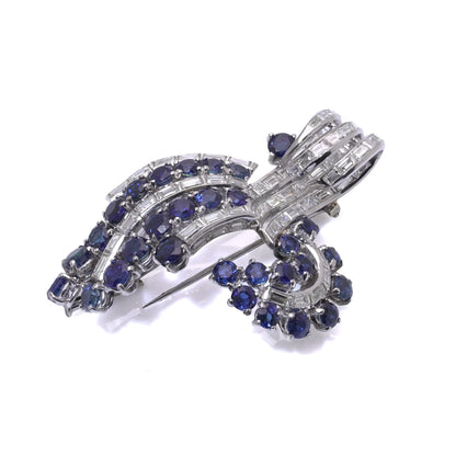 A decorative baguette cut diamond and round sapphire brooch in white metal, on a white background
