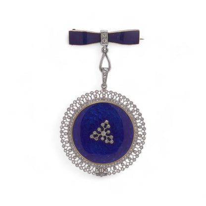 A blue enamel pendant pocket watch in silver with diamonds, suspended by a bow brooch fitting, on a white background