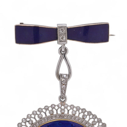 A blue enamel pendant pocket watch in silver with diamonds, suspended by a bow brooch fitting, on a white background
