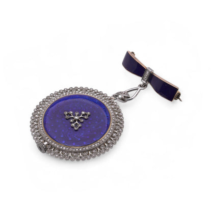 A blue enamel pendant pocket watch in silver with diamonds, suspended by a bow brooch fitting, on a white background