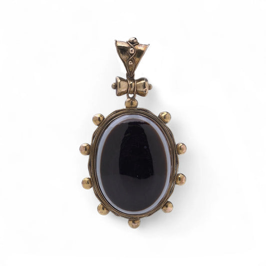 An oval pendant with a cabochon cut banded black agate with yellow gold hobnail bead border, on a white background
