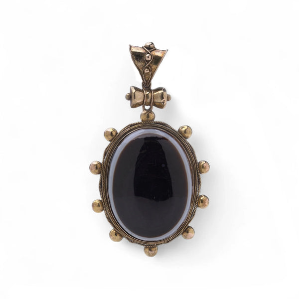 An oval pendant with a cabochon cut banded black agate with yellow gold hobnail bead border, on a white background