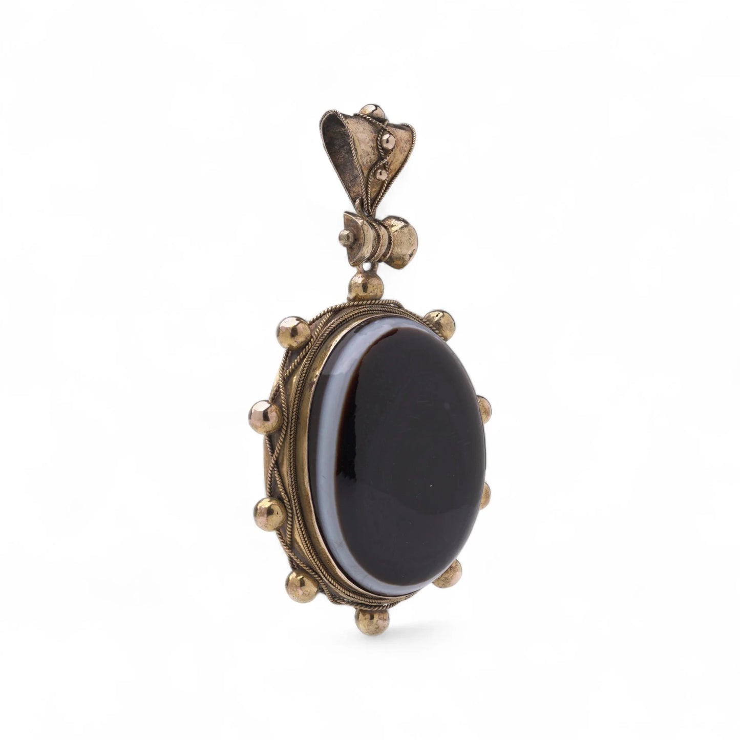 An oval pendant with a cabochon cut banded black agate with yellow gold hobnail bead border, on a white background