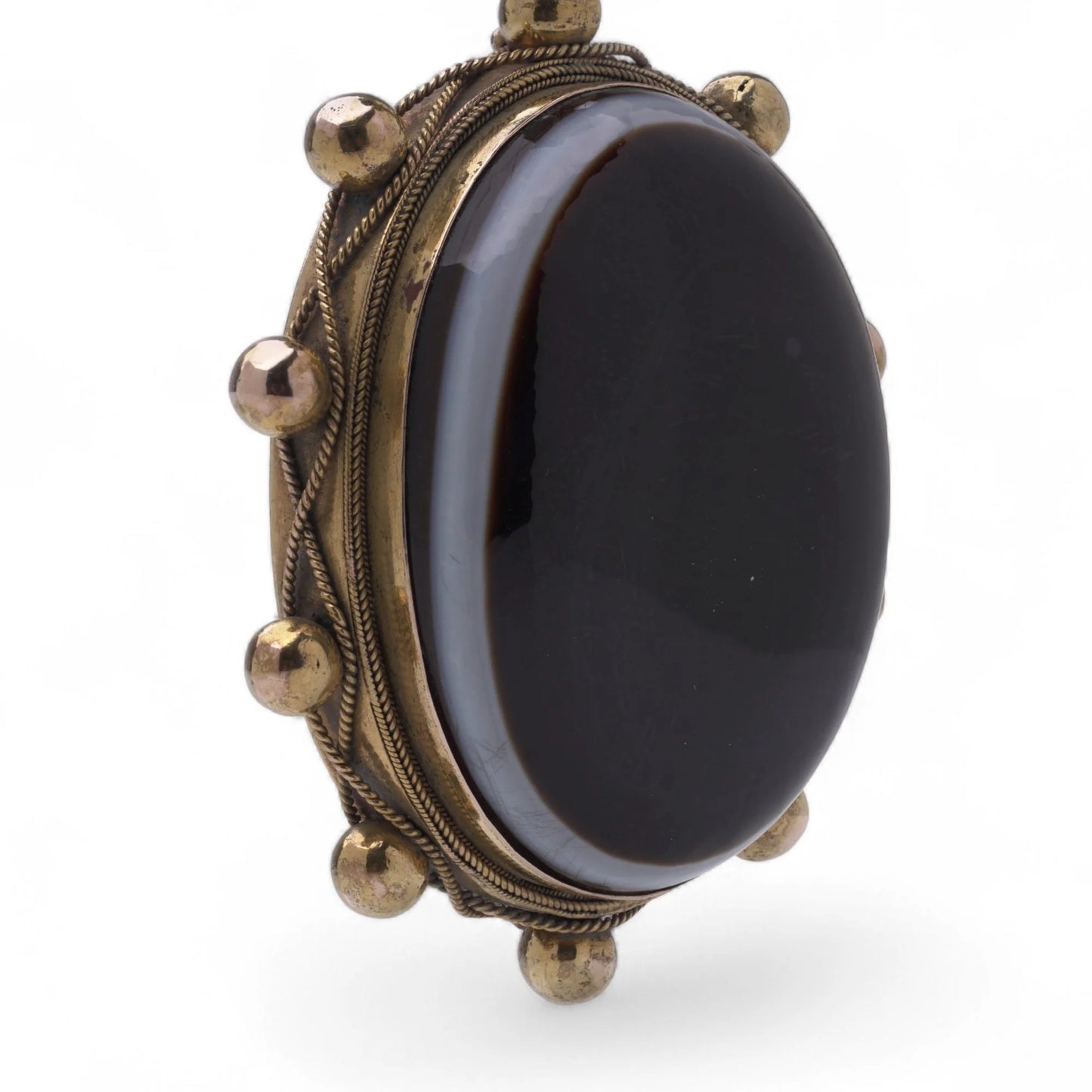 An oval pendant with a cabochon cut banded black agate with yellow gold hobnail bead border, on a white background