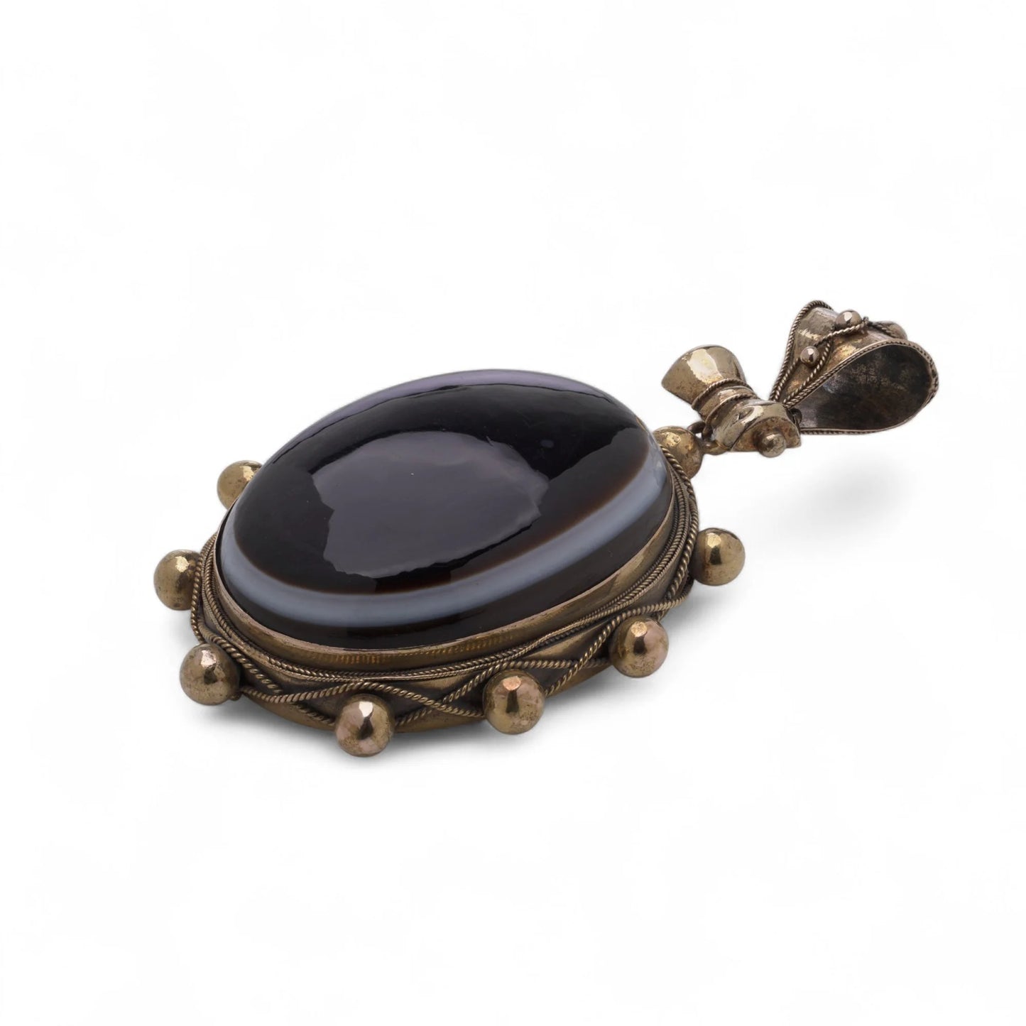 An oval pendant with a cabochon cut banded black agate with yellow gold hobnail bead border, on a white background