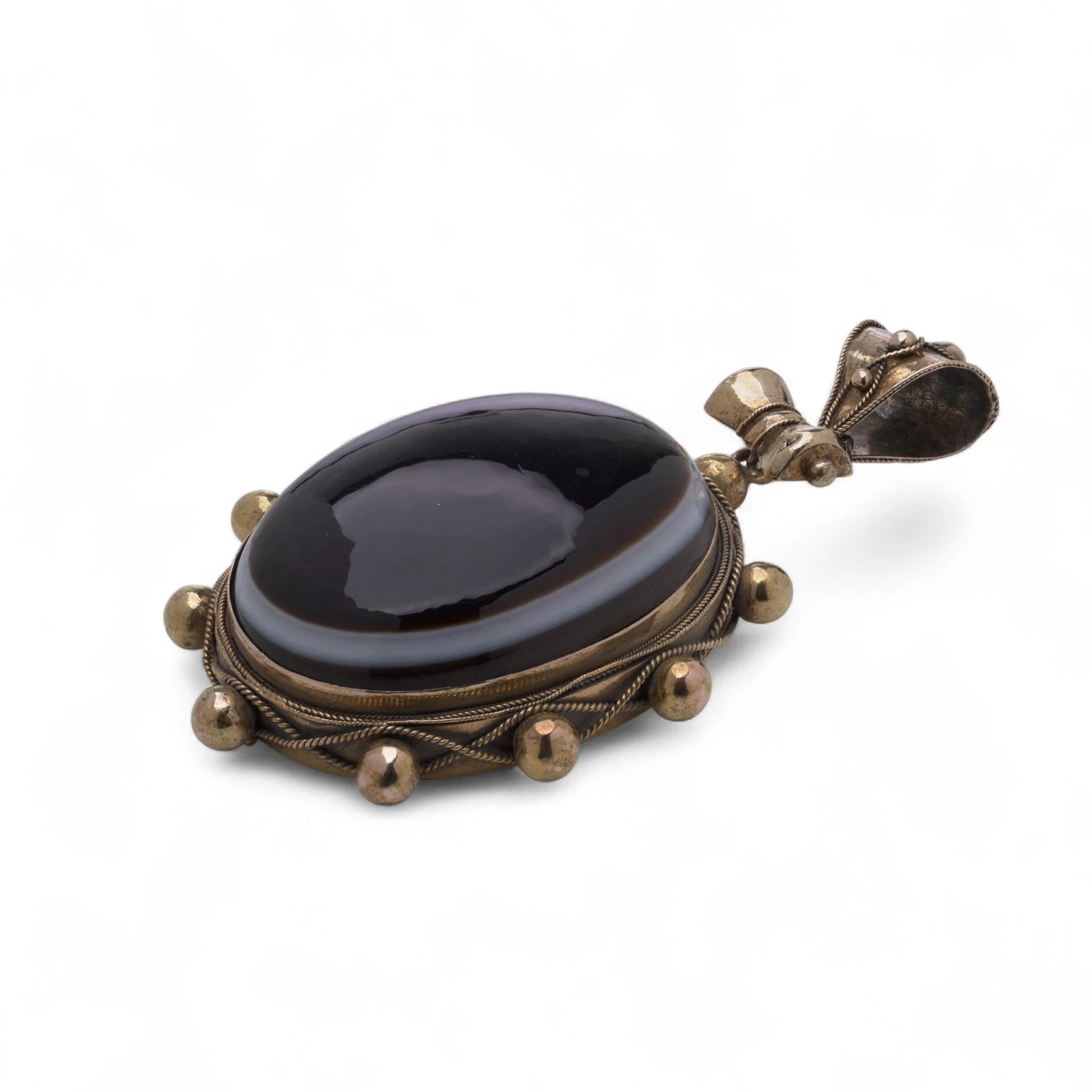 An oval pendant with a cabochon cut banded black agate with yellow gold hobnail bead border, on a white background