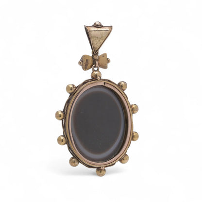 An oval pendant with a cabochon cut banded black agate with yellow gold hobnail bead border, on a white background