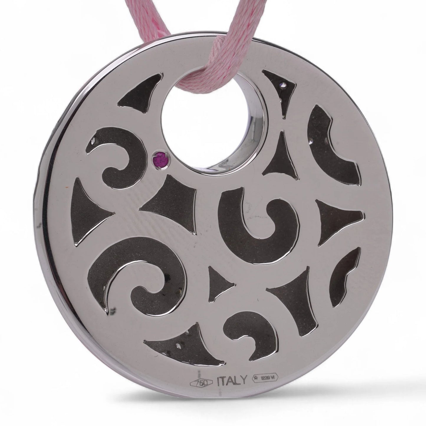 A white gold circular pendant with a cutout design and a pink sapphire, on a pink cord, against a white background