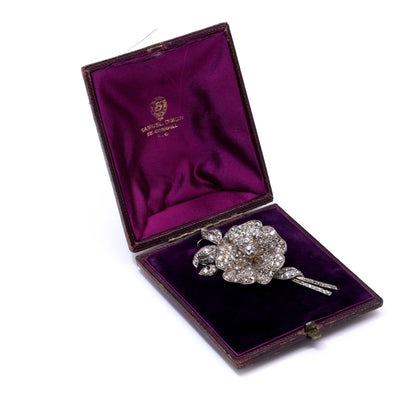 A decorative flower brooch set with diamonds, in silver and gold, in an antique box, on a white background
